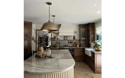 Modern European Kitchen designed by Bre Bertolini, the kitchen features dark stained wood cabinets, and a rounded kitchen island painted in muted white. This kitchen also showcases a bell-shaped Hoodsly range hood that has been plastered using Roman clay.